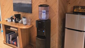 A kitchenette with a refrigerator, a water dispenser, and a wooden console table with books and kitchen appliances.
