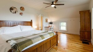 A spacious bedroom with a wooden bed, a ceiling fan, and a large window.