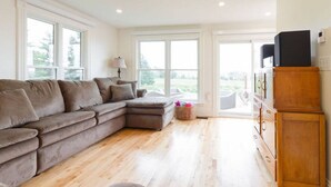 A living room with a sectional sofa, a wooden cabinet, and large windows.