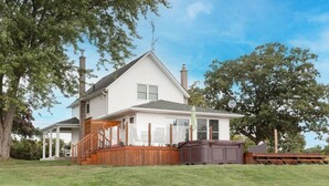 A two-story house with a wooden deck, a covered porch, and a large brown shed in the front yard.
