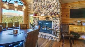A cozy cabin interior with a stone fireplace, wooden walls, a dining area, and a television. - Alma Mountain Getaway w/ Private Hot Tub & Views (Alma)