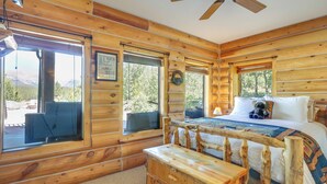 A log cabin bedroom with a bed, wooden bench, and large windows offering a view of the outdoors. - Alma Mountain Getaway w/ Private Hot Tub & Views (Alma)