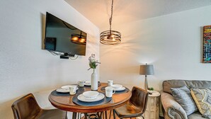 A dining area with a round table, chairs, and a television mounted on the wall. - Fishing Pond & Pier: Secluded Broken Bow Cottage! (Broken Bow)