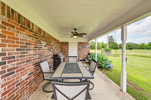 Eine überdachte Terrasse mit Backsteinmauer, Deckenventilator, Tisch mit Stühlen und Grill.