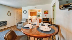 A dining area with a wooden table set for four, a chair, and a kitchen in the background. - Fishing Pond & Pier: Secluded Broken Bow Cottage! (Broken Bow)