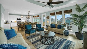A spacious living room with a ceiling fan, a dining area with wooden furniture, and a kitchen with white cabinets. - 5Bed / 5 Baths  Walk 2 Beach!  Arcade!  Ocean View!  Ping Pong! Fire Pit! (Crystal Beach, Texas)