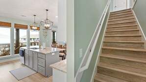 A modern kitchen with a central island, wooden staircase, and large windows. - 5Bed / 5 Baths  Walk 2 Beach!  Arcade!  Ocean View!  Ping Pong! Fire Pit! (Crystal Beach, Texas)