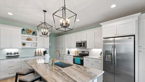 A modern kitchen with white cabinetry, a central island with a sink, and stainless steel appliances including a refrigerator and microwave. - 5Bed / 5 Baths  Walk 2 Beach!  Arcade!  Ocean View!  Ping Pong! Fire Pit! (Crystal Beach, Texas)