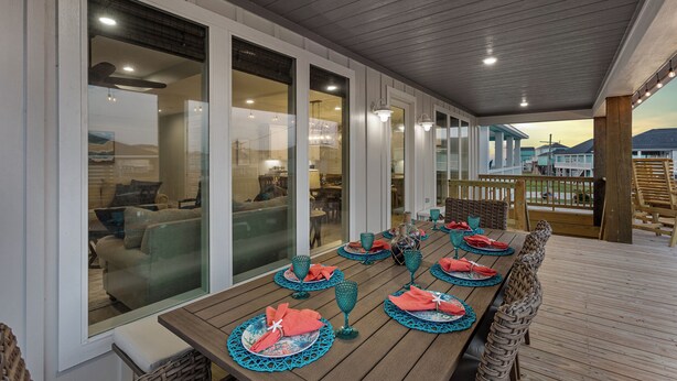 An outdoor dining area with a wooden deck, glass doors leading to an interior space, and a view of the landscape. - 5Bed / 5 Baths  Walk 2 Beach!  Arcade!  Ocean View!  Ping Pong! Fire Pit! (Crystal Beach, Texas)