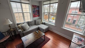 A modern living room with a grey sectional sofa, a wooden coffee table, and large windows offering a view of the city.