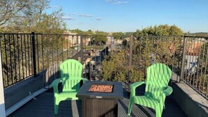Un balcó amb dues cadires verdes i una taula petita, amb vista a una zona residencial plena d'arbres i edificis.