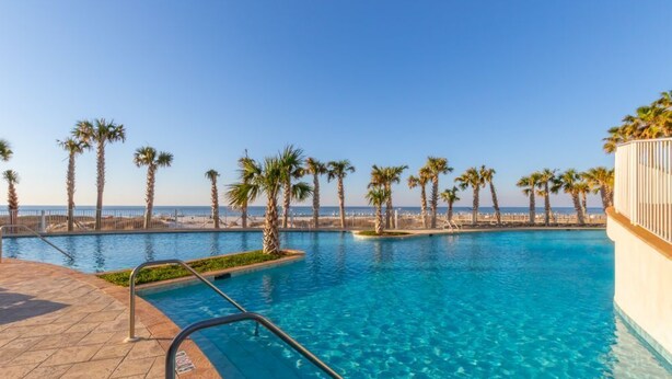 A swimming pool with clear blue water, surrounded by palm trees and a view of the sea.