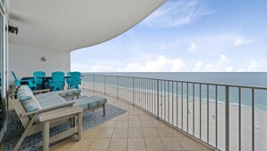 A balcony with a view of the beach, a seating area with chairs and a table, and a railing.