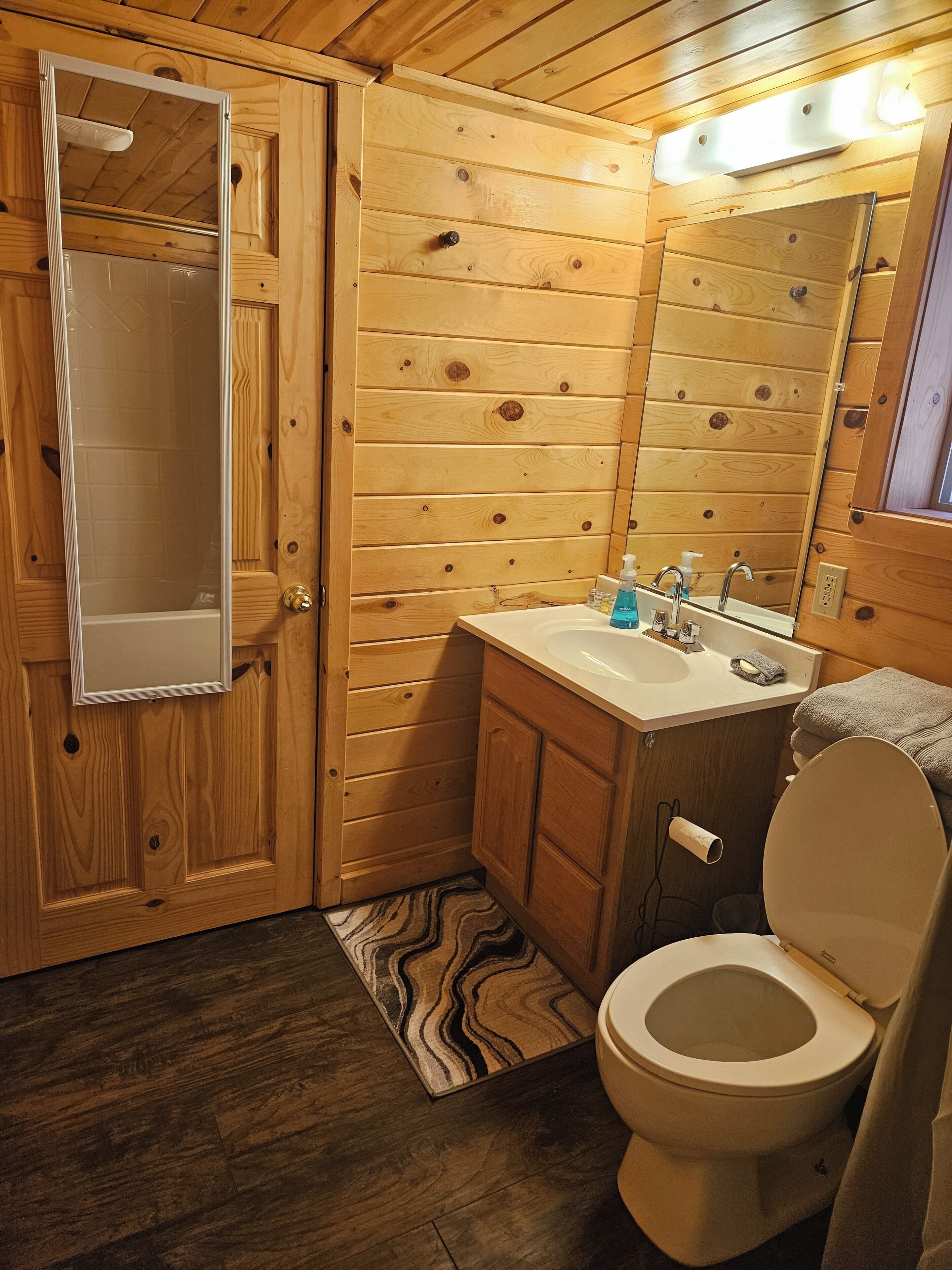 Un baño con paneles de madera, ducha, lavamanos, inodoro y espejo.