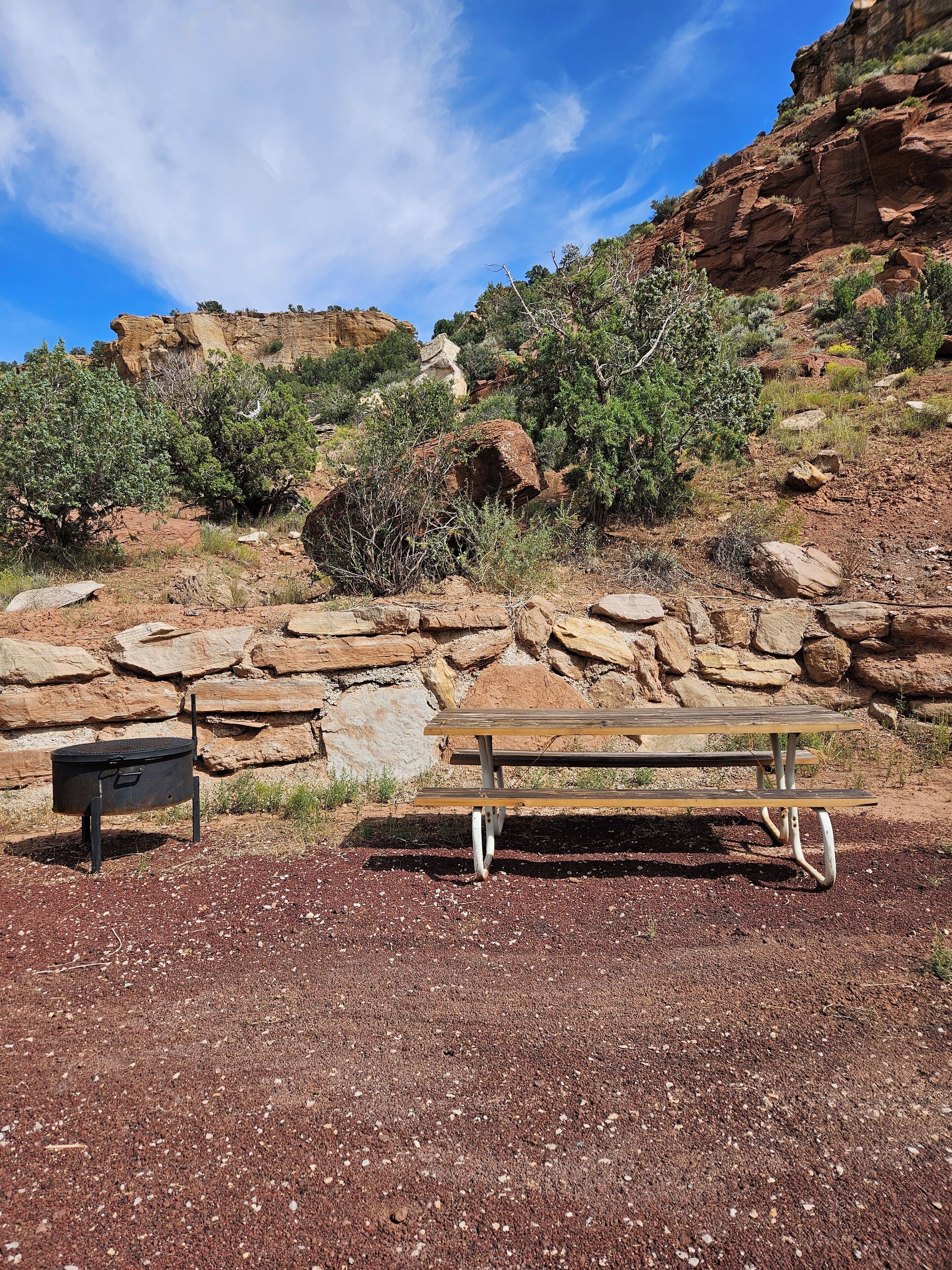 A picnic table in a rocky outdoor setting with a stone wall and sparse vegetation.