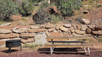 A picnic table in a rocky outdoor setting with a stone wall and sparse vegetation.