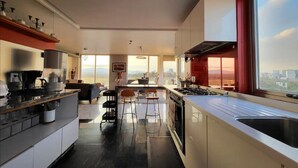 Een moderne keuken met een groot schiereiland, een eetgedeelte met uitzicht, en een stadsgezicht zichtbaar door grote ramen.
