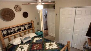 Ein Schlafzimmer mit einem hölzernen Bett, einer Steppdecke, einem Deckenventilator und einem Schrank.
