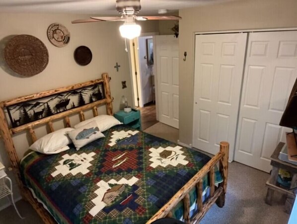 Um quarto com uma cama de madeira, um edredom, um ventilador de teto e um guarda-roupa.