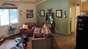 Ein gemütliches Wohnzimmer mit einem Karomuster-Sofa, einem kleinen Tisch mit Lampe und einem Deckenventilator.