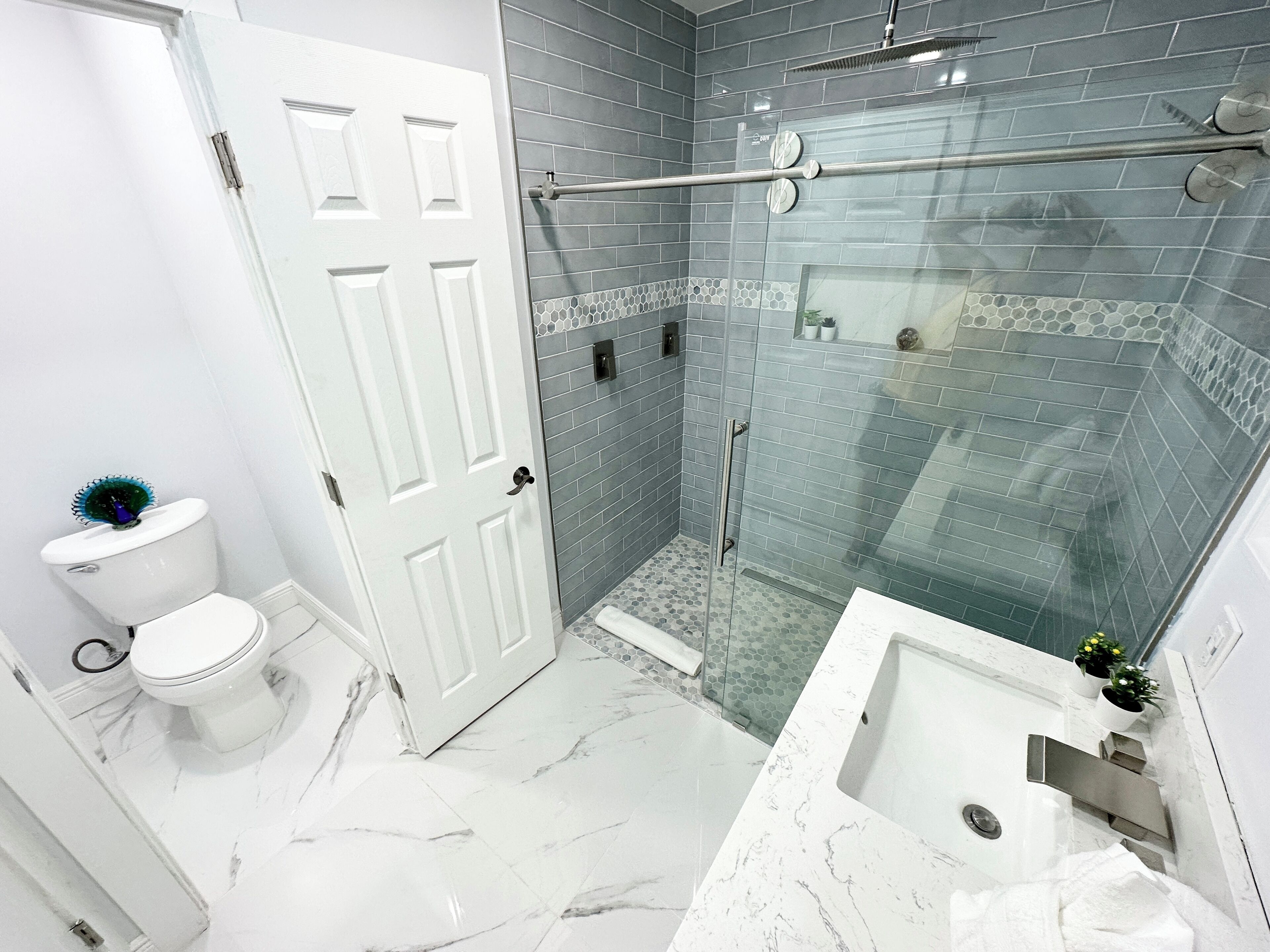 Une salle de bain avec des toilettes blanches, une douche en verre et un lavabo blanc doté d’un plan de toilette en marbre.