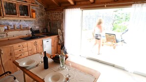 Une table de salle à manger en bois, mise avec des assiettes, des couverts et une bouteille, avec un mur en pierre et des meubles en bois en arrière-plan.