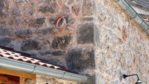 Un bâtiment en pierre avec un toit en métal, une porte à volets verts et deux lampes fixées au mur.
