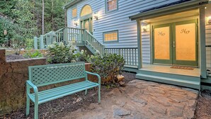 Une maison avec un chemin en pierre, un banc vert et un escalier en bois menant à une porte sur laquelle est inscrit le nom « Hew ».