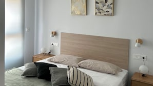 A modern bedroom with a wooden headboard, a bed with multiple pillows, bedside tables with lamps, and two framed artworks on the wall. - Perfect, Modern Studio In The Heart Of Alicante (Alicante (Alacant))