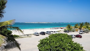 A beach view with parked cars and palm trees. - Apartment sea view Orient bay beach (Saint-Martin)