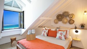 A bedroom with a large window, a bed with orange bedding, and a wall decorated with hats. - Apartment sea view Orient bay beach (Saint-Martin)