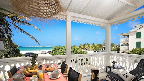 A balcony with a table set for breakfast, overlooking a beach and ocean. - Apartment sea view Orient bay beach (Saint-Martin)