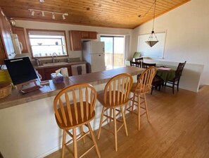 Una cocina con armarios de madera, un refrigerador, una mesa de comedor con sillas y una ventana con persianas.