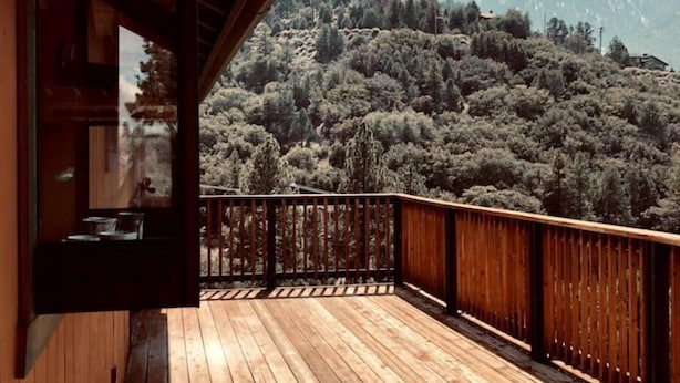 A wooden deck with a view of a forested hillside. - Mountain Getaway with Expansive Beautiful Views (Pine Mountain Club)