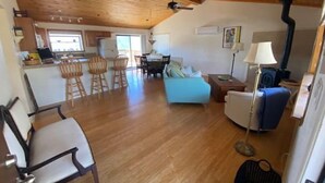 A spacious living area with a kitchen, dining area, and a blue sofa. - Mountain Getaway with Expansive Beautiful Views (Pine Mountain Club)