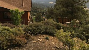 A rustic cabin with a brick chimney, surrounded by dense forest and mountains in the background. - Mountain Getaway with Expansive Beautiful Views (Pine Mountain Club)