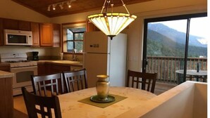 A kitchen with wooden cabinets, a microwave, stove, and a dining area with a table and chairs. - Mountain Getaway with Expansive Beautiful Views (Pine Mountain Club)