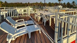 Une terrasse dotée de chaises longues et de tables blanches, entourée d’une balustrade blanche.