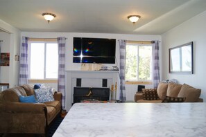 A living room with a flat-screen TV, a fireplace, two sofas, and a large marble table.