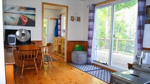A cozy room with a wooden floor, a dining table with chairs, a green cushioned bench, a window with curtains, and a view of trees.