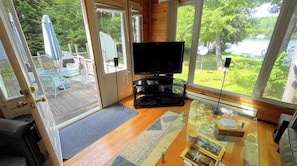 Una habitación con una televisión sobre una mesa de vidrio, una puerta que da al exterior y vistas a un lago.