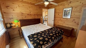 Une pièce aux murs lambrés, comprenant un lit, une table de chevet, une lampe et un ventilateur de plafond.