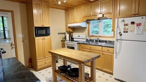 Una cocina con armarios de madera, un refrigerador blanco, un microondas, una estufa y una mesa de madera.