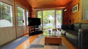 A wooden interior with a television, a glass coffee table, and a leather sofa.
