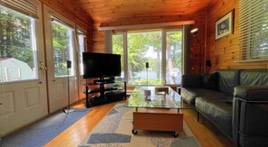 A wooden interior with a television, a glass coffee table, and a leather sofa. - Great Value! Lasswade Lake Cottage Rental (North Kawartha)