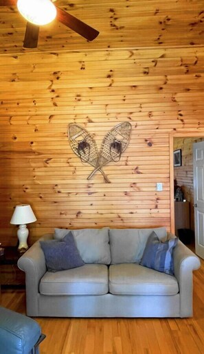 A cozy room with wooden walls, a ceiling fan, a sofa, and a lamp. - Great Value! Lasswade Lake Cottage Rental (North Kawartha)