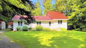 A white house with a red roof, surrounded by lush greenery and trees.