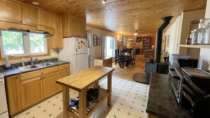 A wooden cabin-style kitchen with a central island, a stove, and a dining area with chairs.