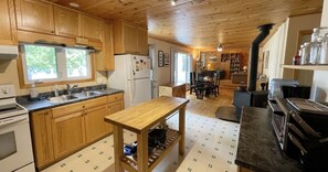 A wooden cabin-style kitchen with a central island, a stove, and a dining area with chairs. - Great Value! Lasswade Lake Cottage Rental (North Kawartha)
