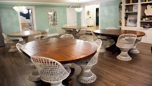 A dining area with round wooden tables and white wicker chairs, a chandelier, and a white cabinet with shelves. - McKinley Mansion Half Building, sleeps 35, Gym, Arcade Room (Pocatello)